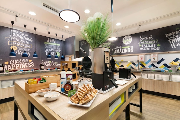 A modern cafe with a counter displaying waffles and breakfast items, motivational wall art, and a clean, organized layout.