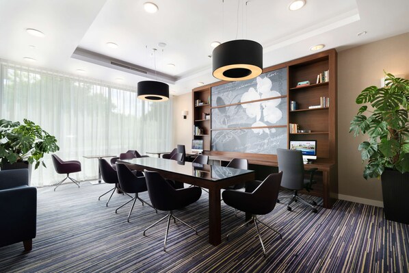 A modern conference room with a large table, black chairs, a bookshelf, and a large window with sheer curtains. - Hampton by Hilton Krakow (Kraków)