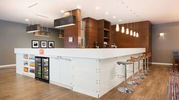 Uma área de bar moderna com balcão branco, várias luminárias pendentes e um dispensador de bebidas refrigerado.