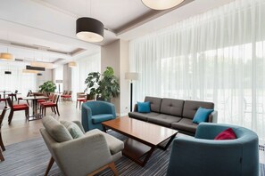 A modern hotel lobby with a seating area, large windows, and a dining space. - Hampton by Hilton Krakow (Kraków)