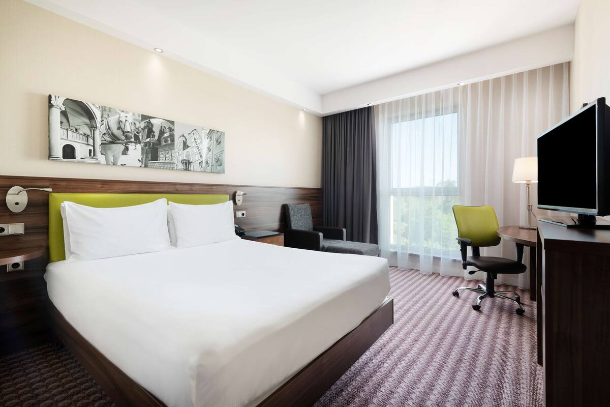 A hotel room with a large bed, a desk with a computer, a chair, and a TV.