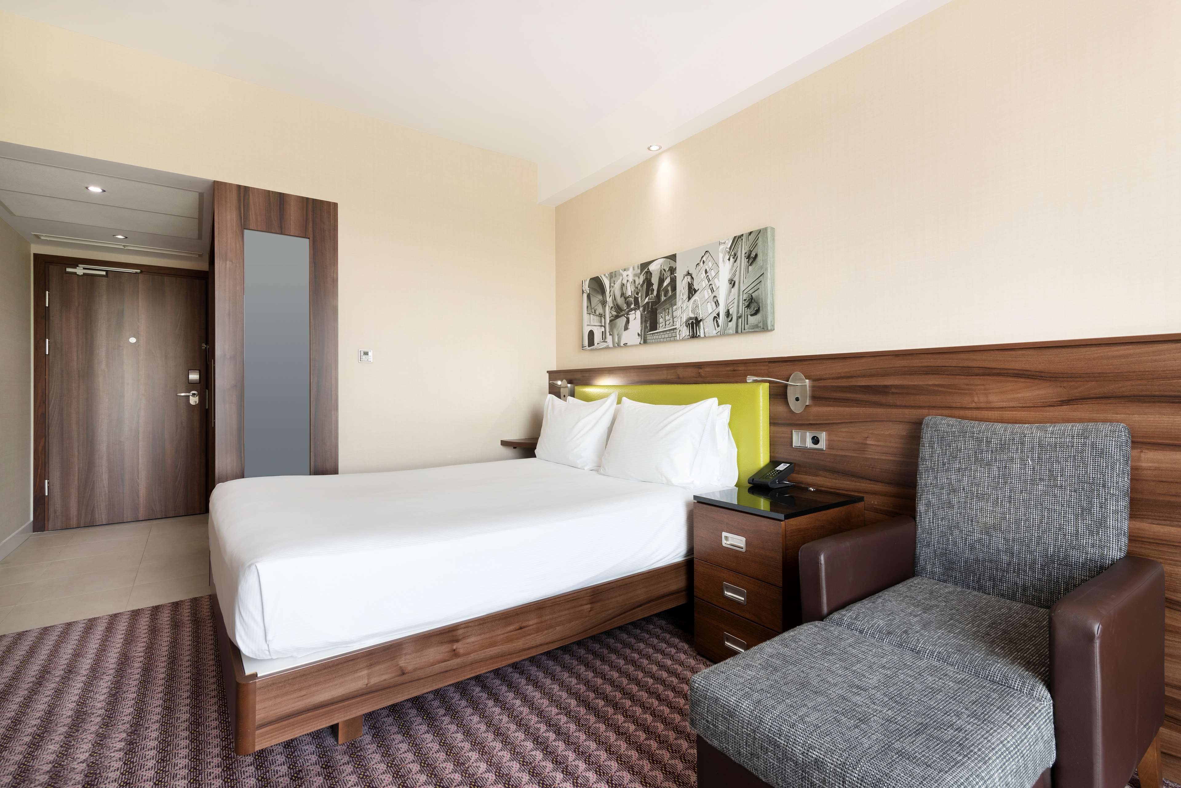 Una habitación de hotel con cama, mesita de noche con teléfono, una silla y una obra de arte colgada en la pared.