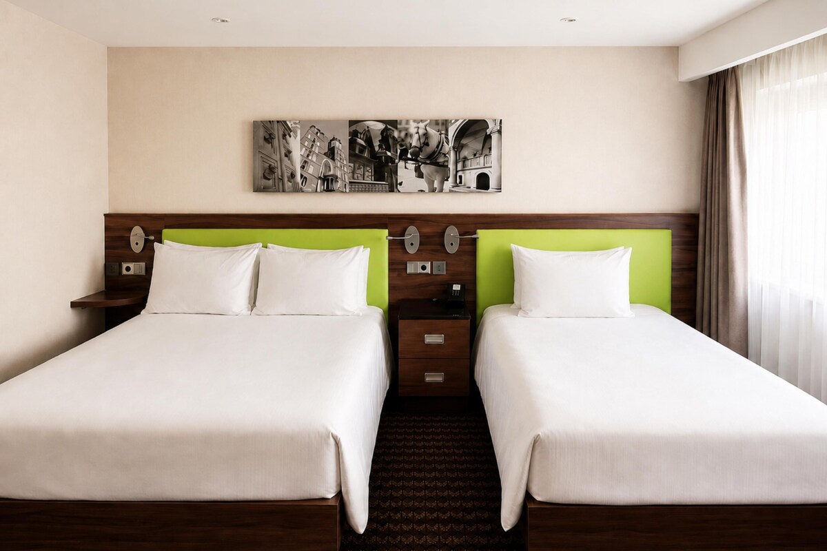 A hotel room with two beds, a nightstand, a telephone, and a wall-mounted artwork.
