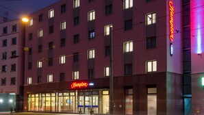 Un hotel Hampton con fachada moderna, varios ventanales y un llamativo letrero de neón.