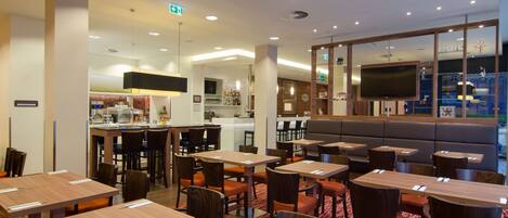A hotel lobby with multiple seating areas, a bar, and a television screen.