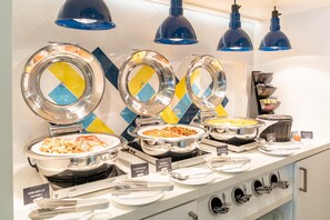 A buffet setup with labeled food stations including meatballs, baked beans, and grilled vegetables. - Hampton by Hilton Nuremberg City Centre (Nuremberg)