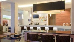 Un área de bar moderna con una barra larga, varios taburetes y una pantalla de televisión.