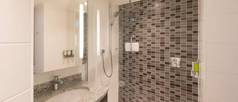 Un baño moderno con lavamanos de granito, ducha con cerramiento de vidrio y pared cubierta de azulejos con diseño de mosaico.