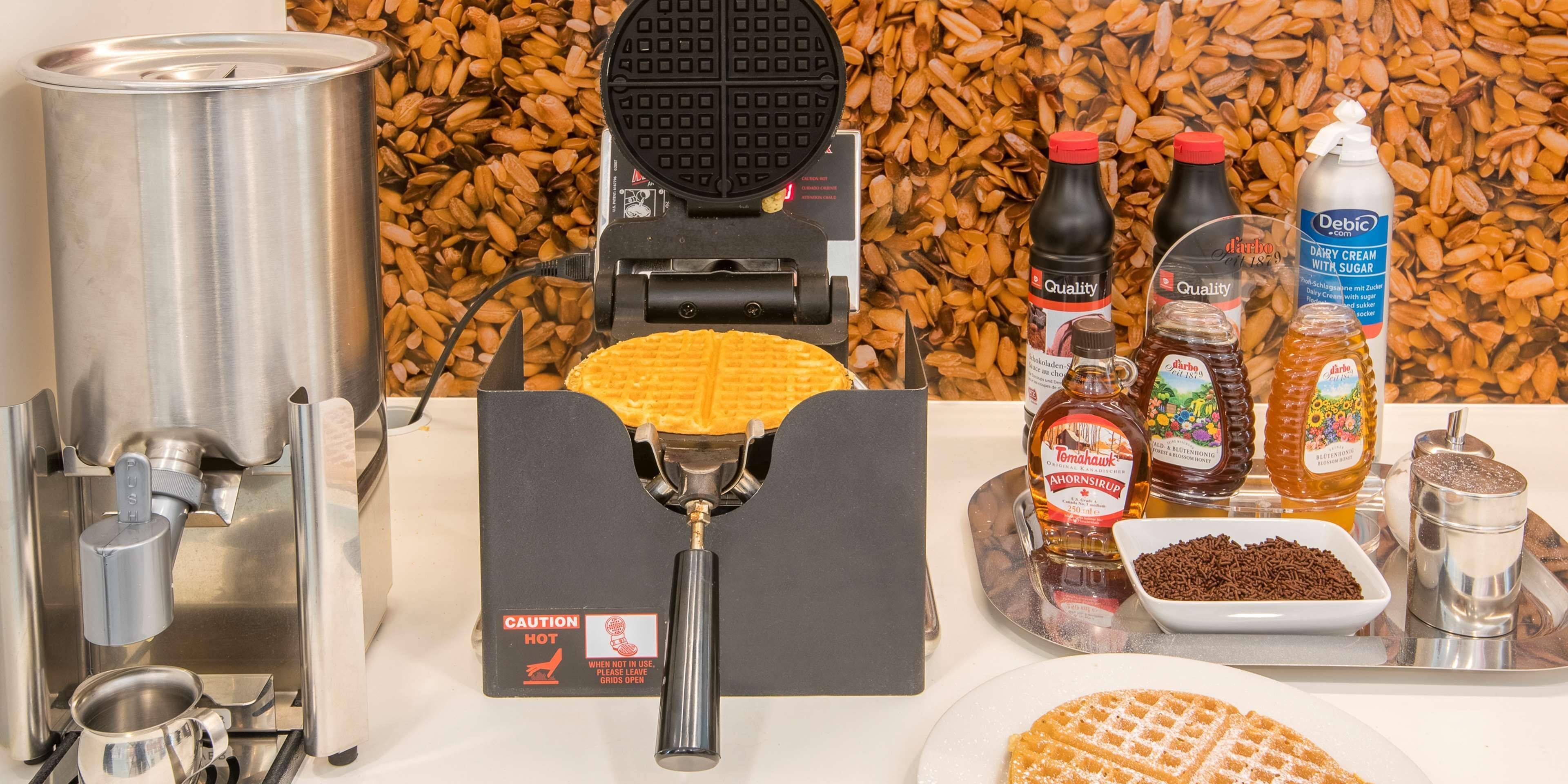 Una máquina para gofres, un gofre y diferentes condimentos sobre una bandeja.