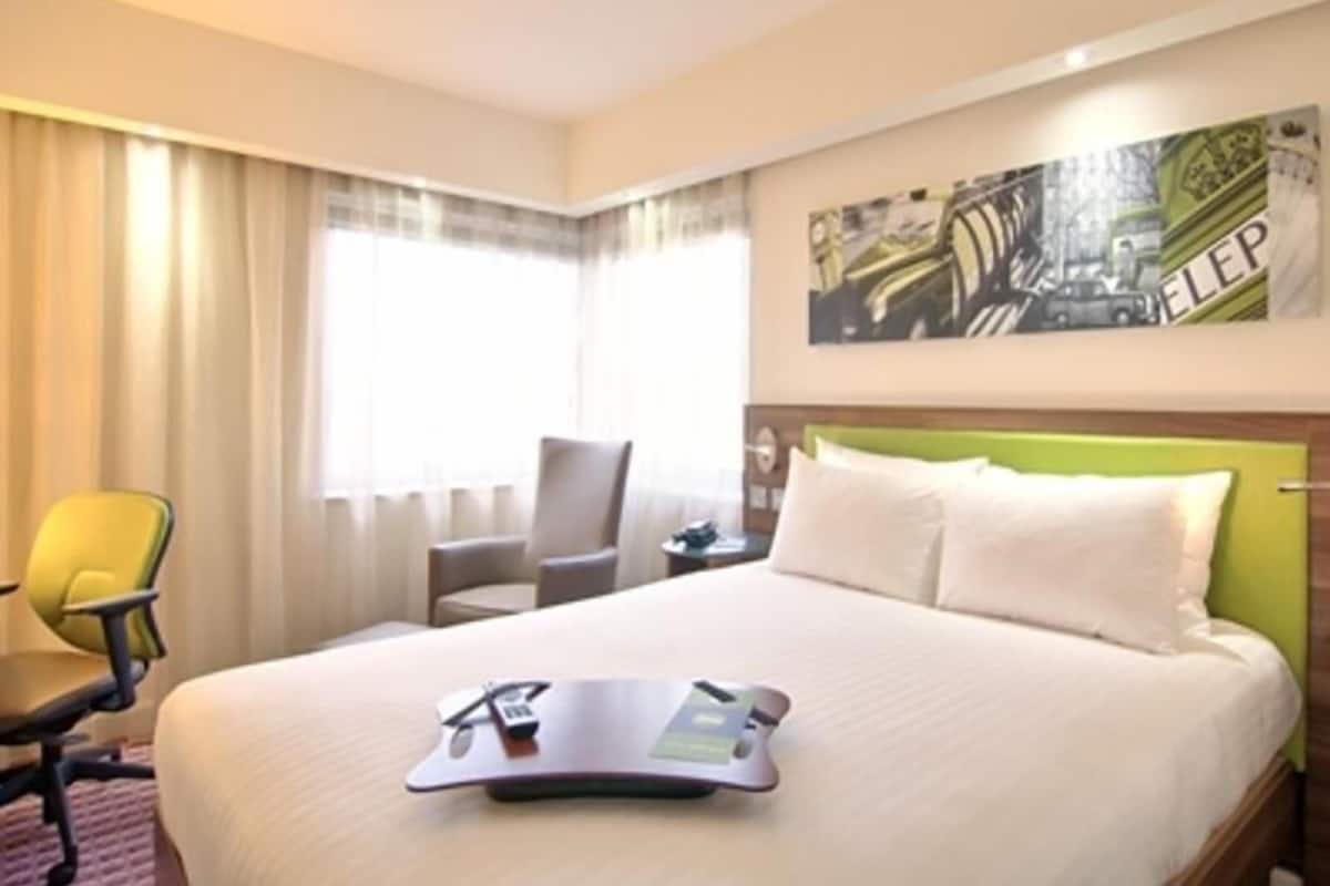 Una habitación de hotel con cama, una silla, un escritorio y una ventana con cortinas.