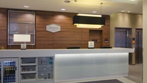 Un mostrador de recepción moderno de hotel con un panel de pared de madera, una vitrina con artículos de cortesía y un letrero que indica 'Hilton Honors'.