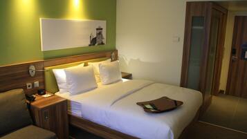 Une chambre d’hôtel avec un lit en bois, du linge de lit blanc, une table de chevet avec une lampe et un mur vert orné d’un tableau.