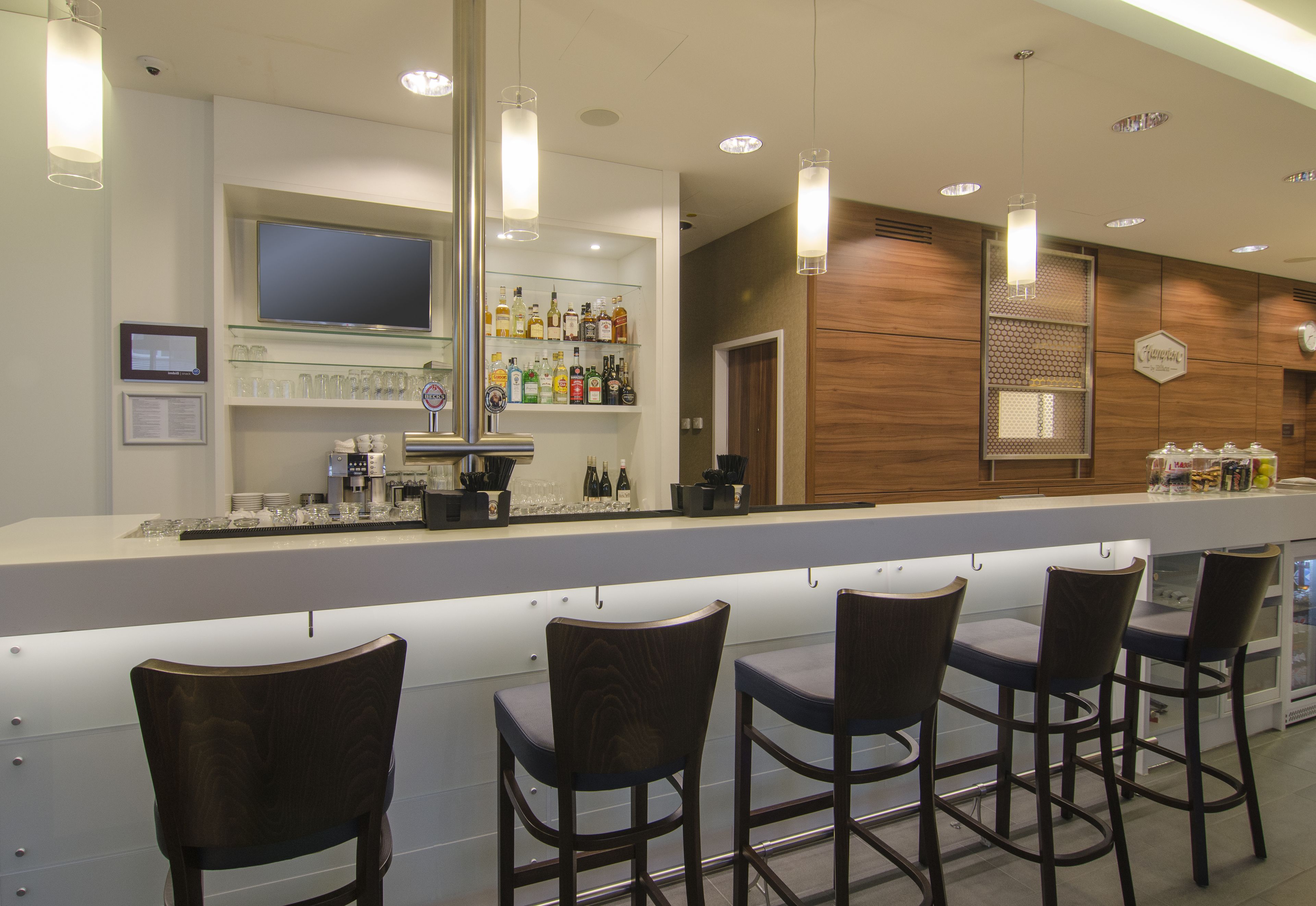 A bar area with a long counter, bar stools, a television, and shelves with bottles.