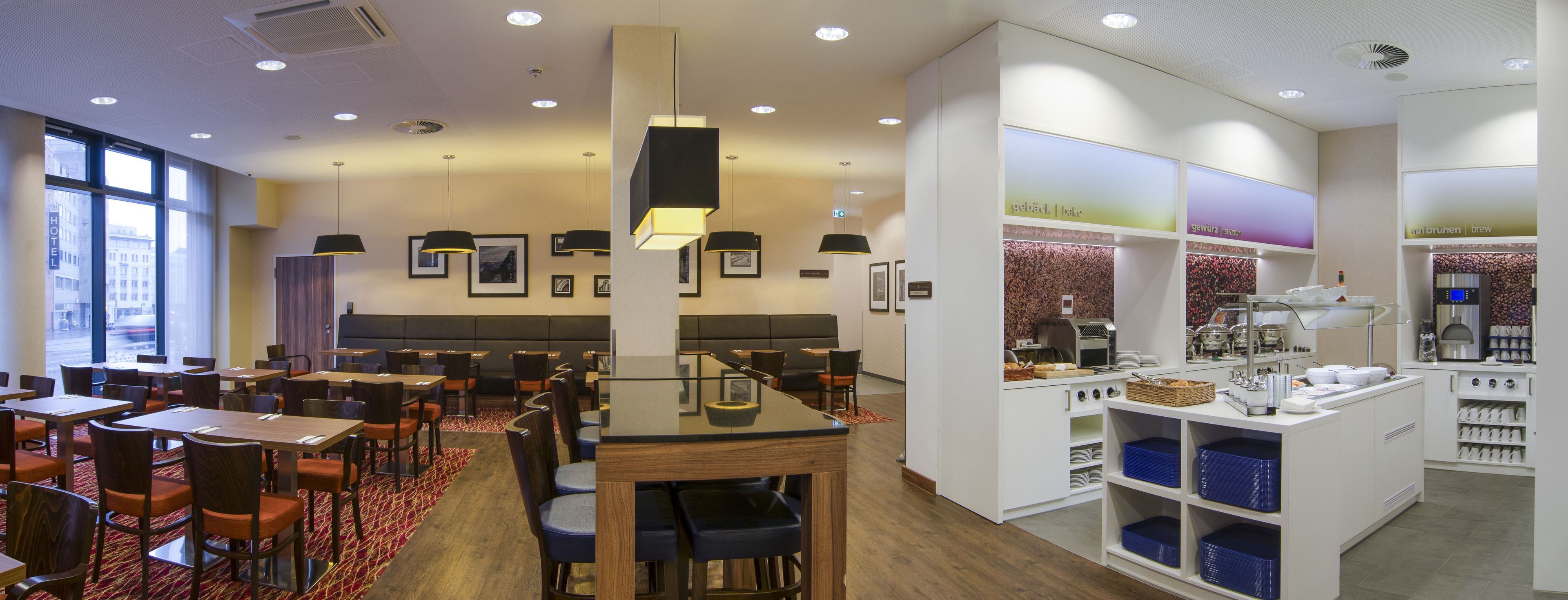 A hotel restaurant with multiple dining tables and chairs, a buffet area, and a coffee station.