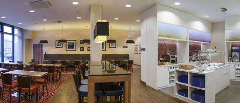 A hotel restaurant with multiple dining tables and chairs, a buffet area, and a coffee station.