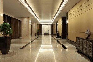 Un hall de hotel con un largo pasillo, una recepción y una planta grande en maceta.