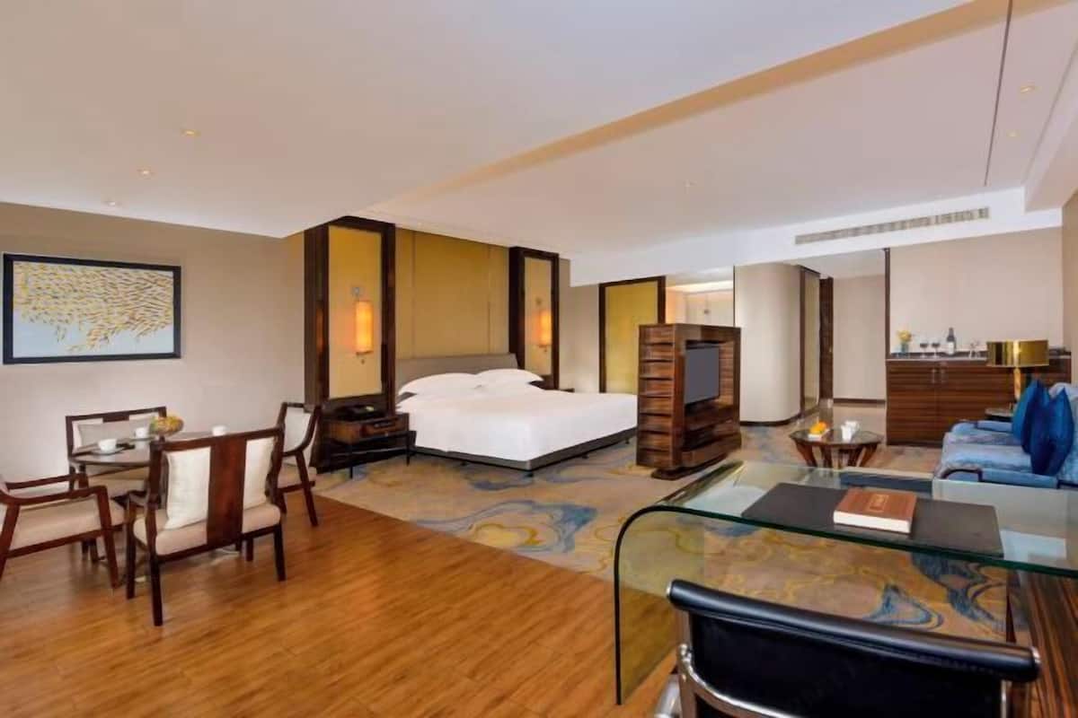 A hotel room with a bed, a desk, a chair, a sofa, and a glass coffee table.