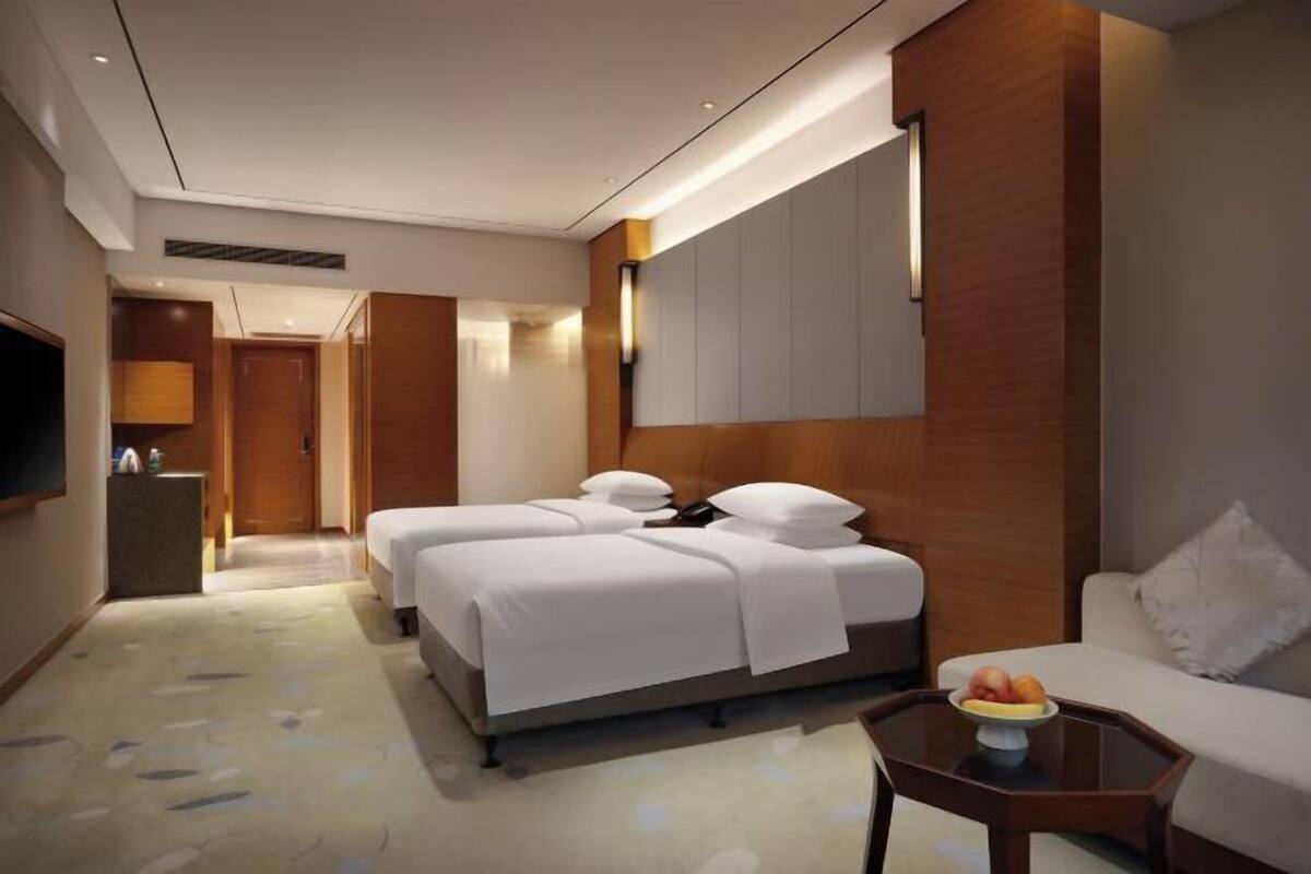 A hotel room with two beds, a sofa, a small table with fruit, and a TV.