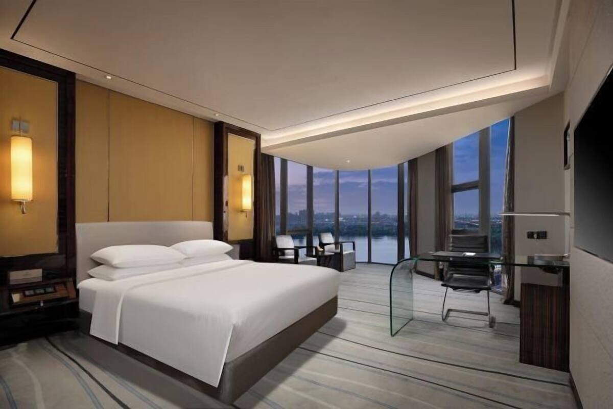 A modern hotel room with a large bed, a desk, and a view of the city.