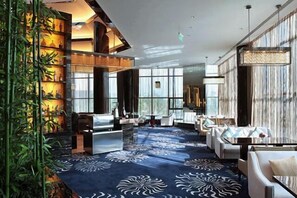 Un amplio vestíbulo de hotel con alfombra estampada, zona de estar y ventanas grandes.