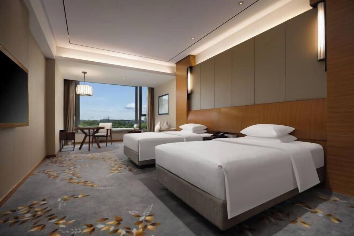 A hotel room with two beds, a desk, and a view of the city.