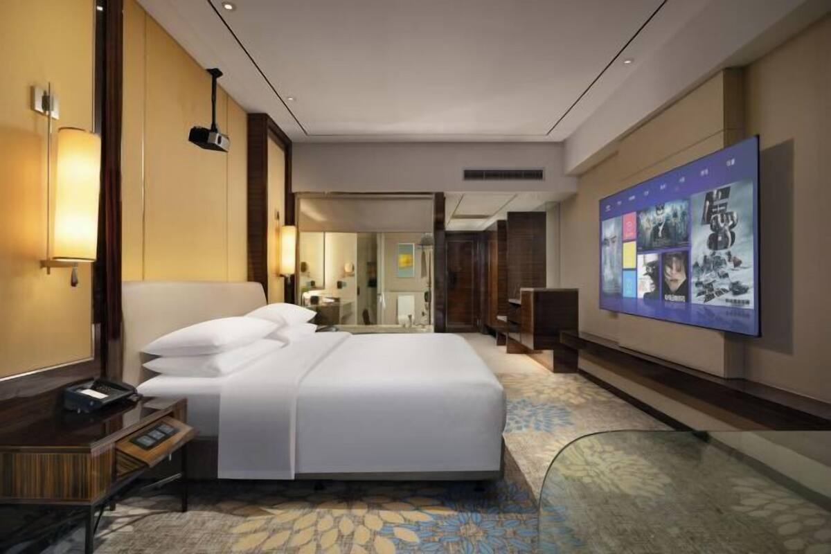 A hotel room with a large bed, bedside tables, a desk, and a large poster on the wall.