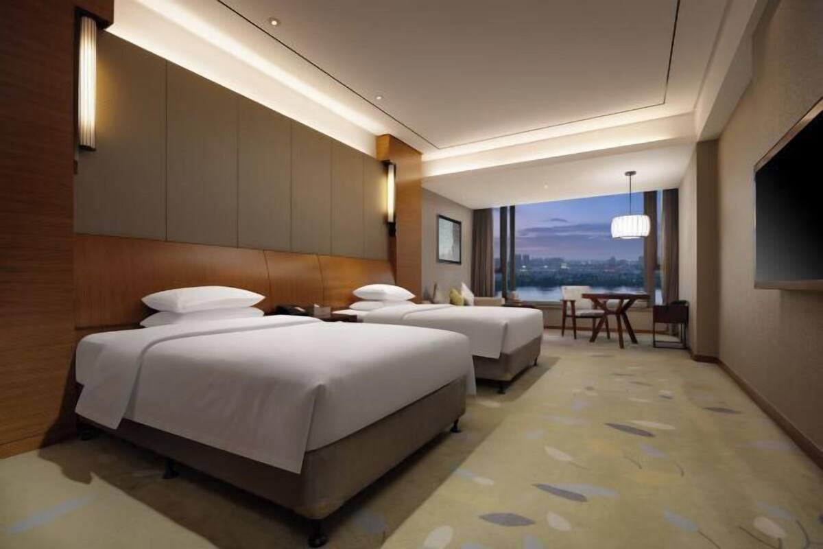 A hotel room with two beds, a dining area, a TV, and a city view.