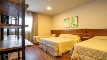 Habitación de hotel con tres camas individuales, piso de madera, cabecero de madera y un escritorio con silla.