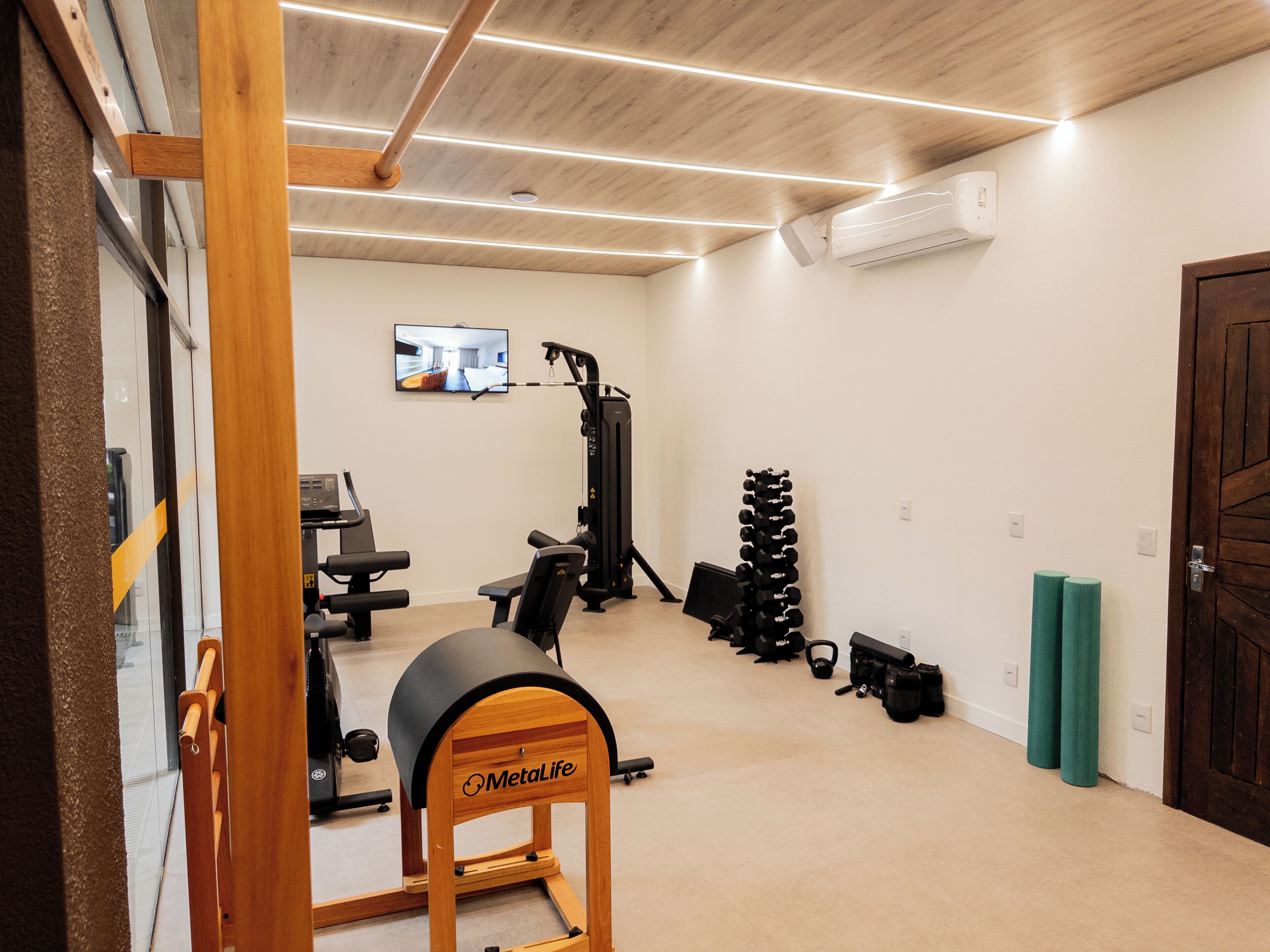 Ein Heim-Fitnessraum mit Trainingsgeräten, einem Fernseher und einer Holztür.