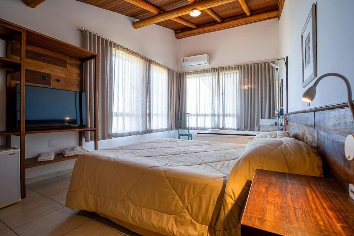 Quarto de hotel com uma cama grande, uma mesa, uma TV e um ar condicionado.