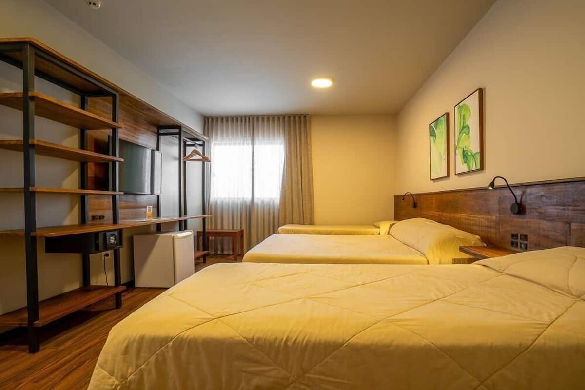 Quarto de hotel com duas camas, uma escrivaninha, uma cadeira e uma televisão.