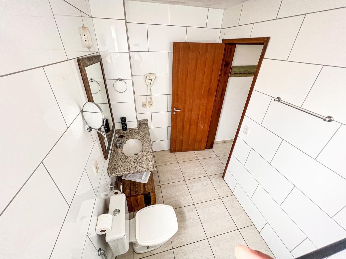 A bathroom with white tiled walls, a wooden door, a sink with a mirror, and a toilet.