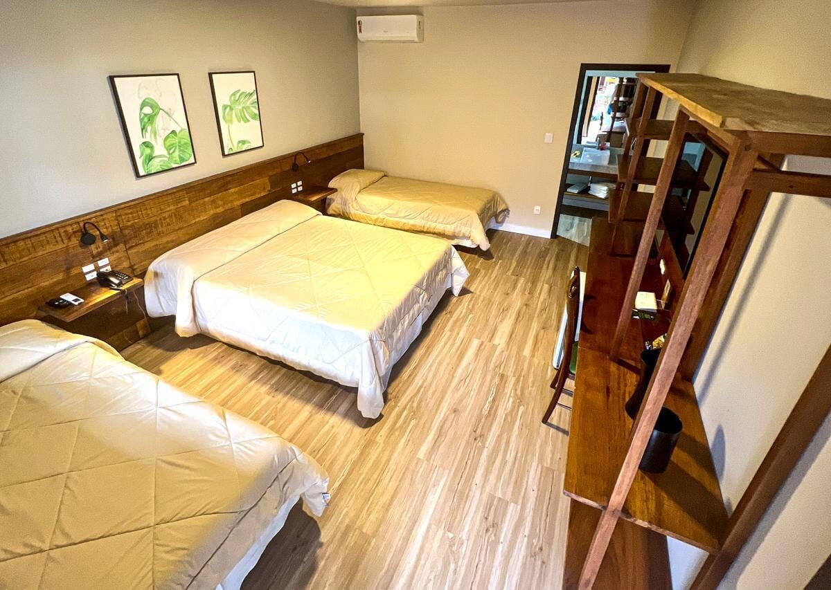 Een hotelkamer met twee bedden, houten vloeren, een houten kledingkast en twee foto's in lijsten aan de muur.