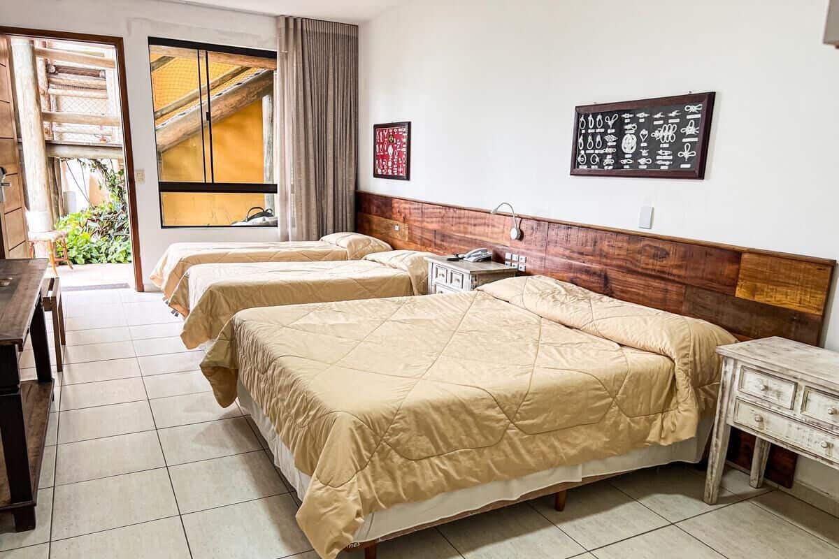 Quarto de hotel com duas camas, cabeceira de madeira, uma escrivaninha e uma cadeira.