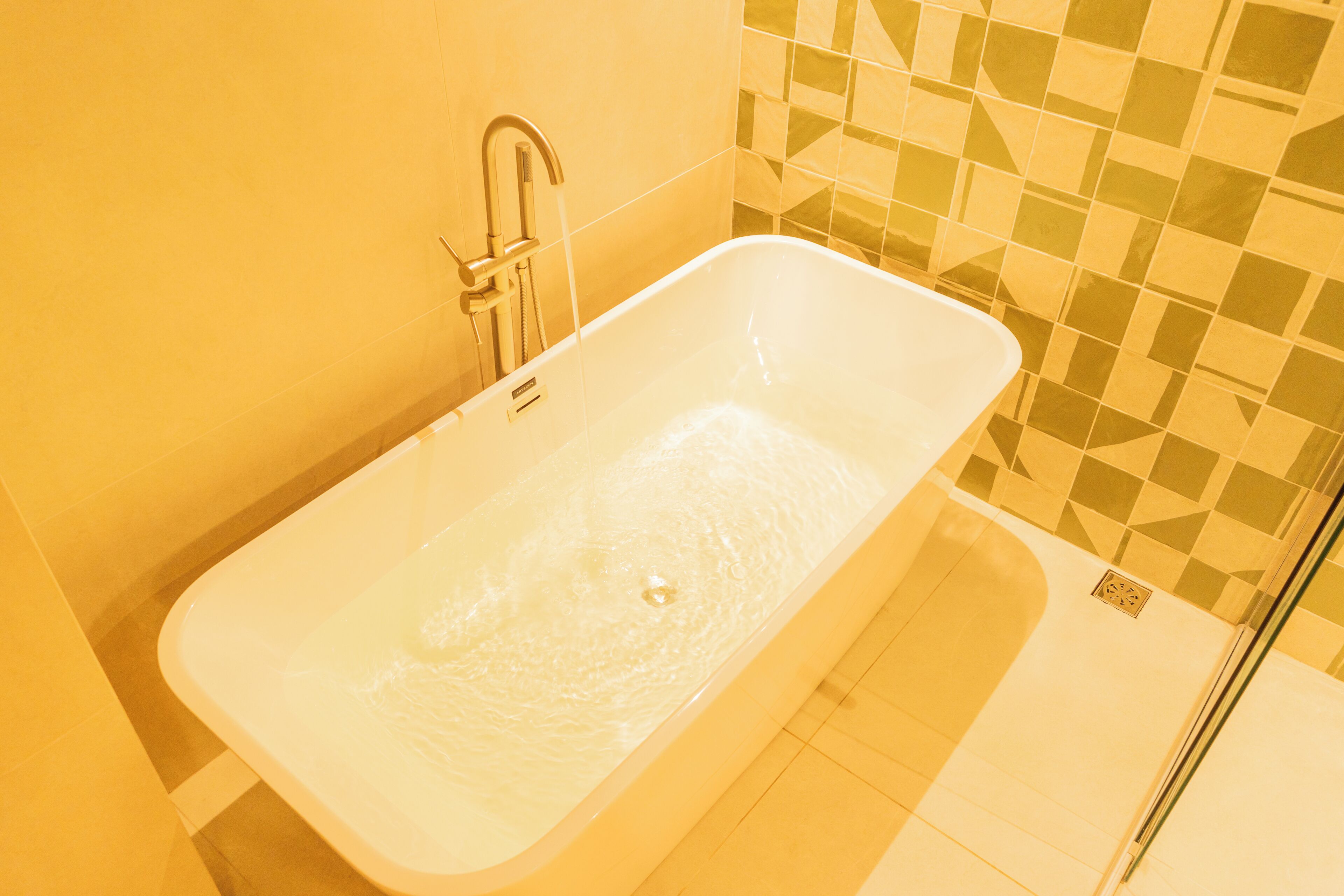 A bathroom with a white bathtub, a shower area, and a tiled wall.