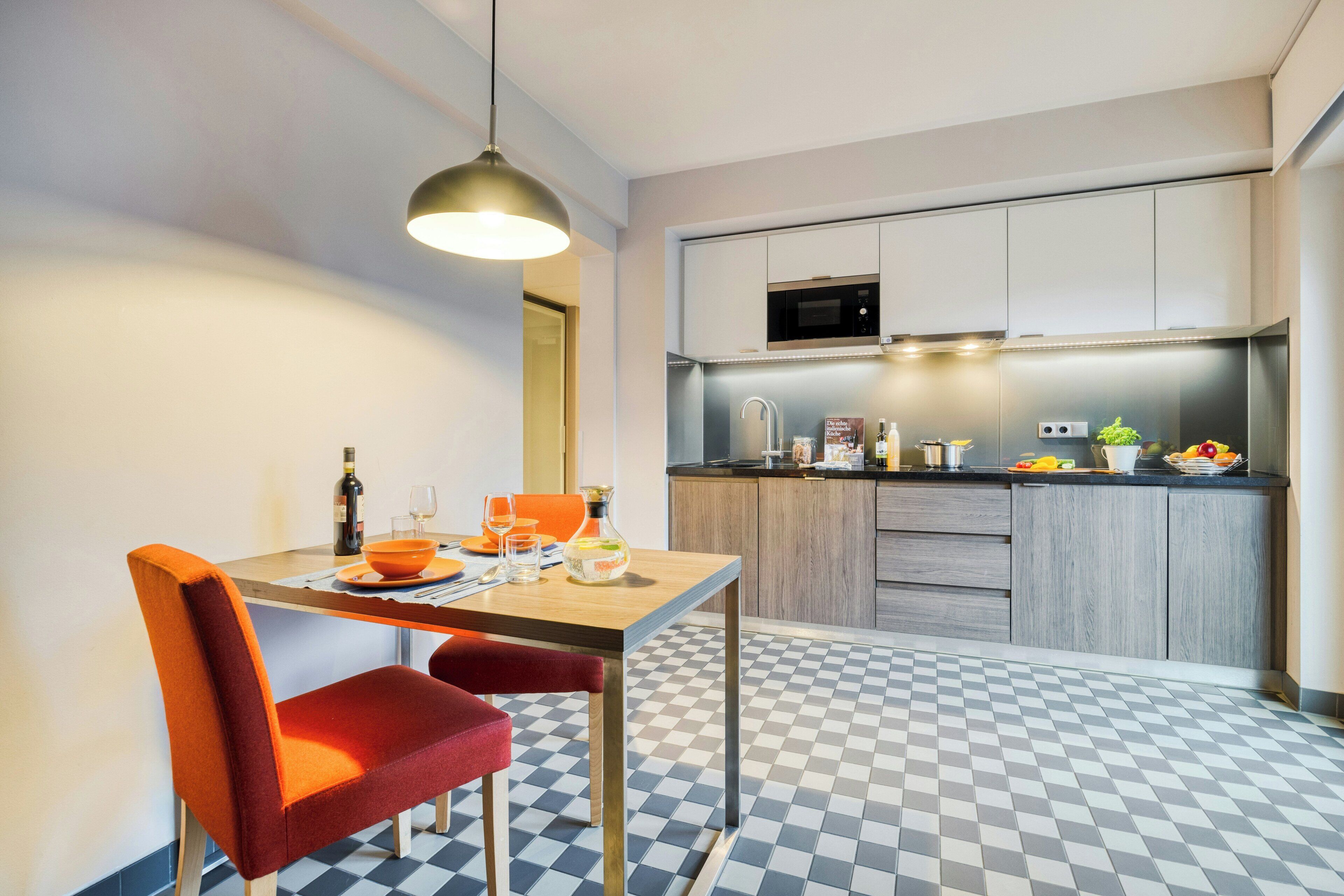 A modern kitchen with a checkered floor, a dining table with chairs, and a pendant light.