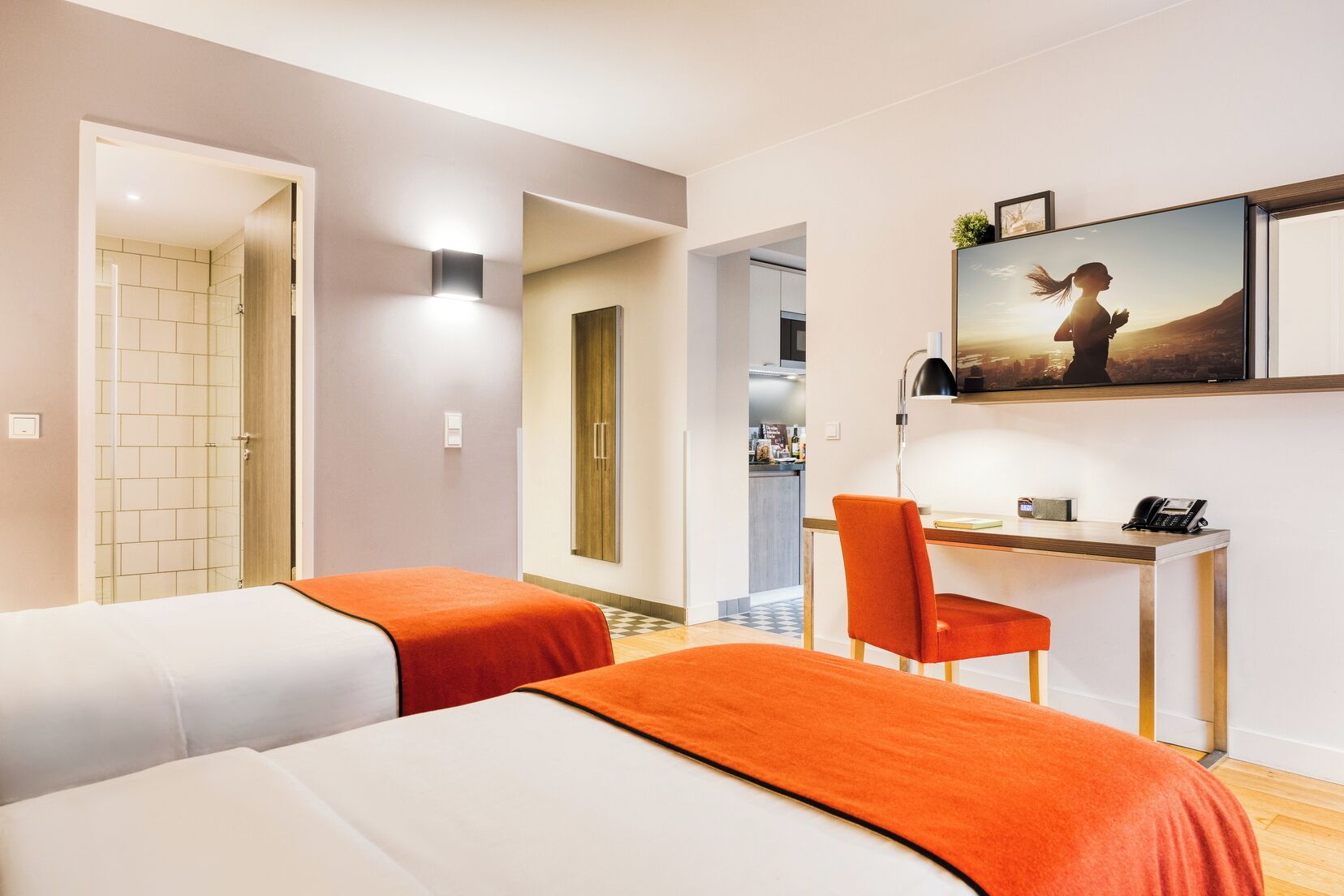 A hotel room with two beds, a desk, a chair, a phone, and a painting on the wall.