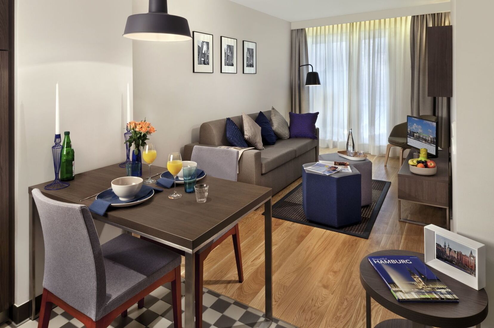 A modern hotel room with a dining area, a sofa, a TV, and a magazine on the table.