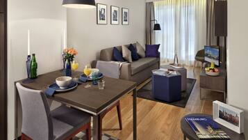 A modern hotel room with a dining area, a sofa, a TV, and a magazine on the table.