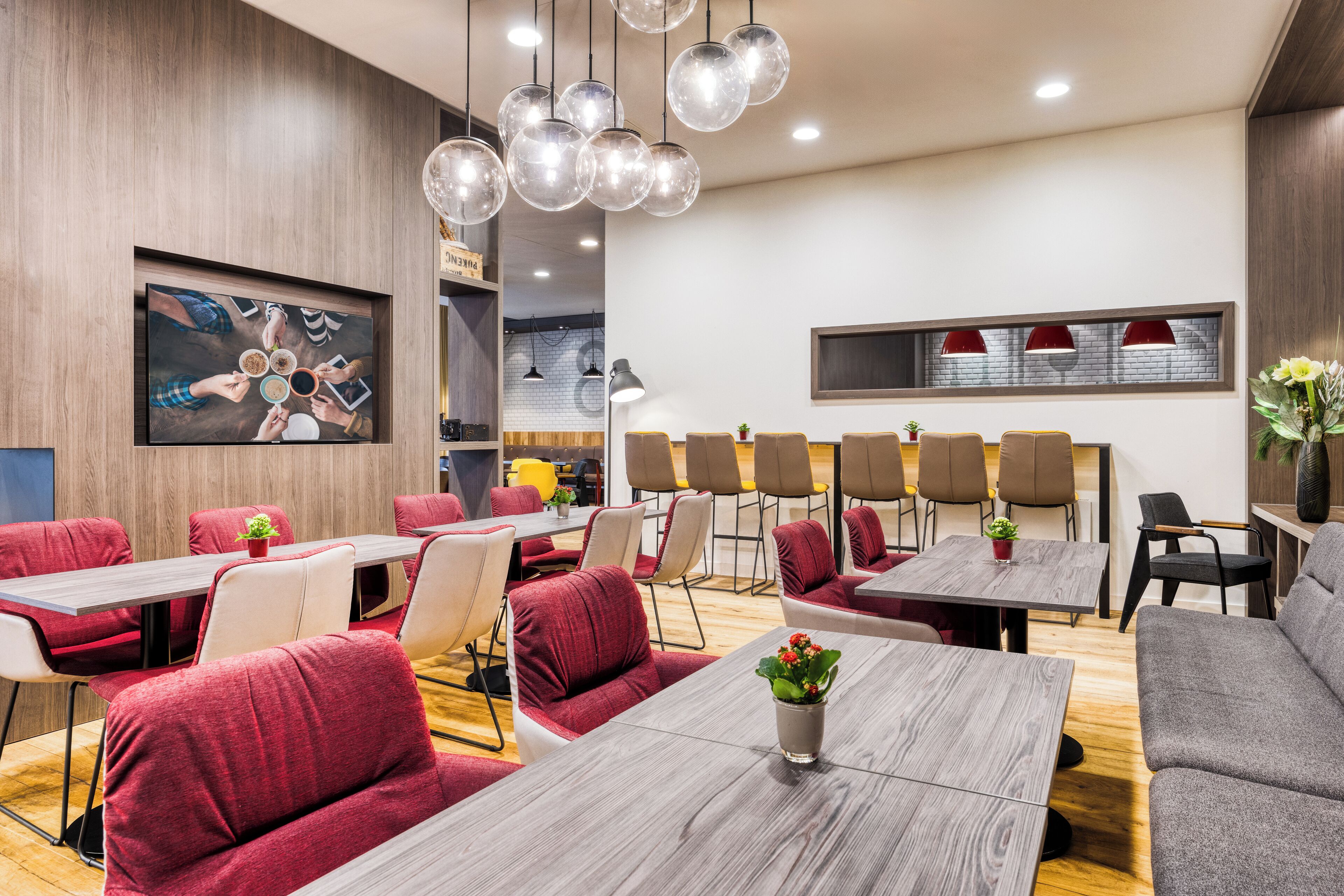 A modern conference room with wooden tables, red and grey upholstered chairs, and pendant lighting.