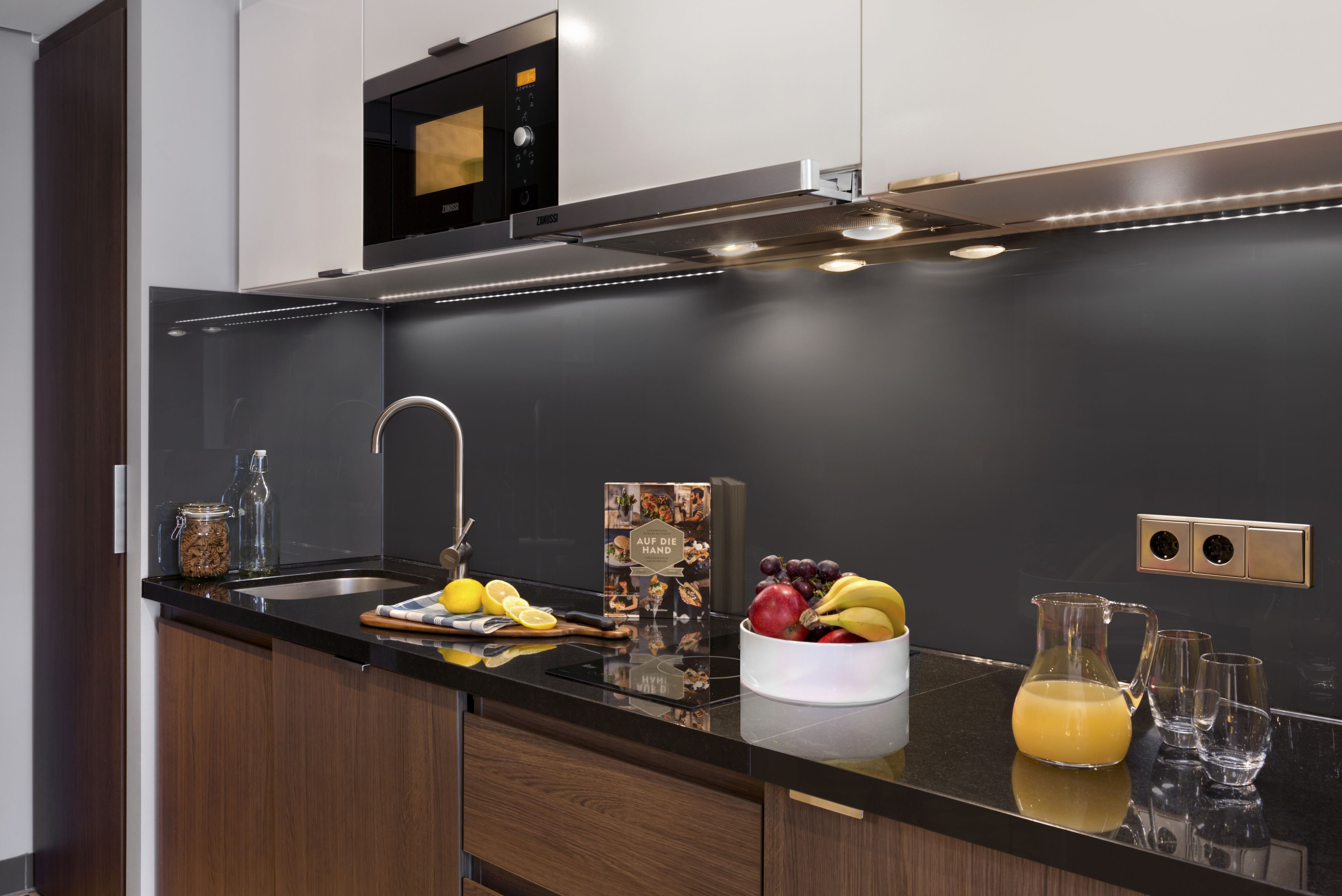 A modern kitchen with a black countertop, stainless steel appliances, and a fruit bowl.