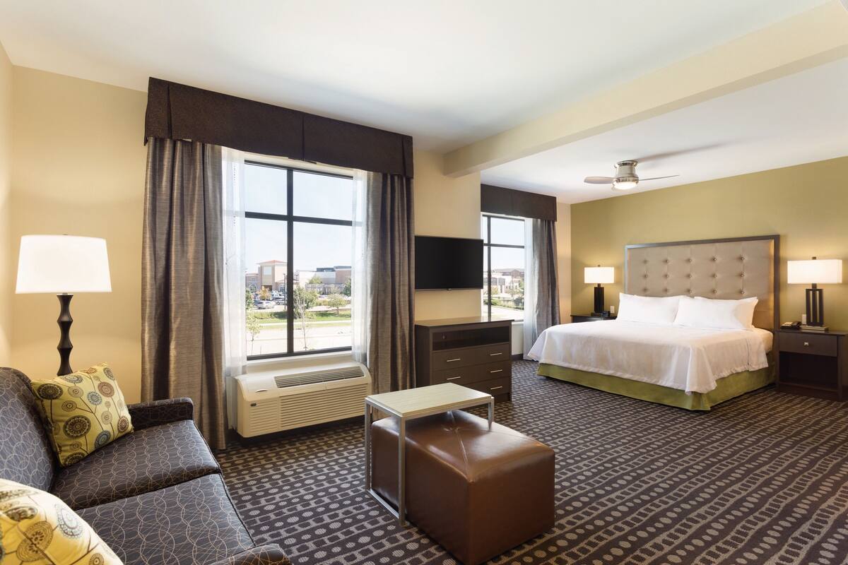 A hotel room with a bed, a sofa, a small table, a TV, and a ceiling fan.