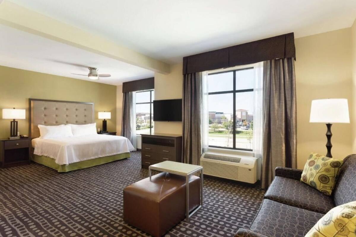 A hotel room with a bed, a sofa, a small table, a TV, a heater, and a window with curtains.