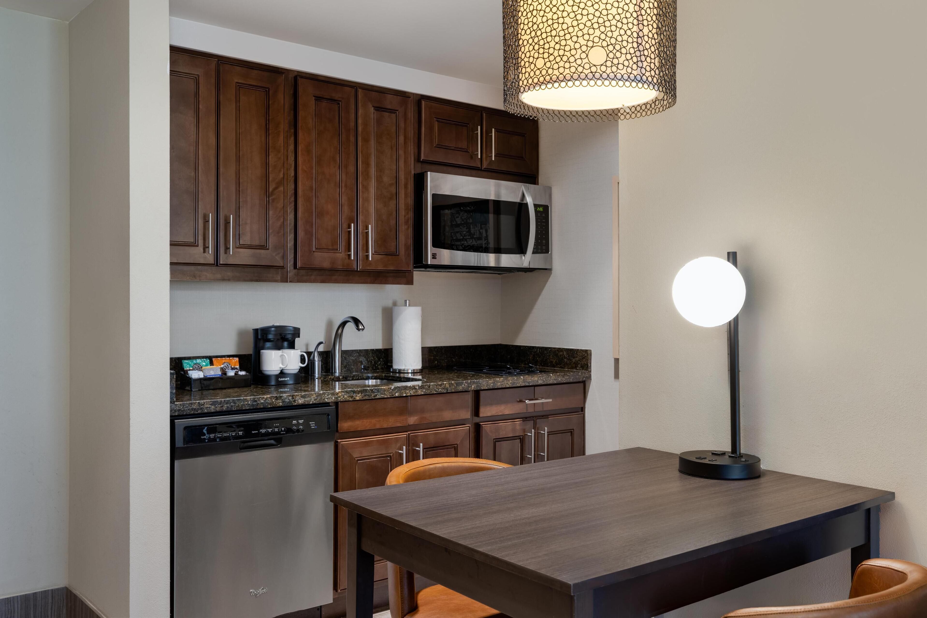 A modern kitchen with dark wooden cabinets, a stainless steel microwave, a dishwasher, and a table with chairs.
