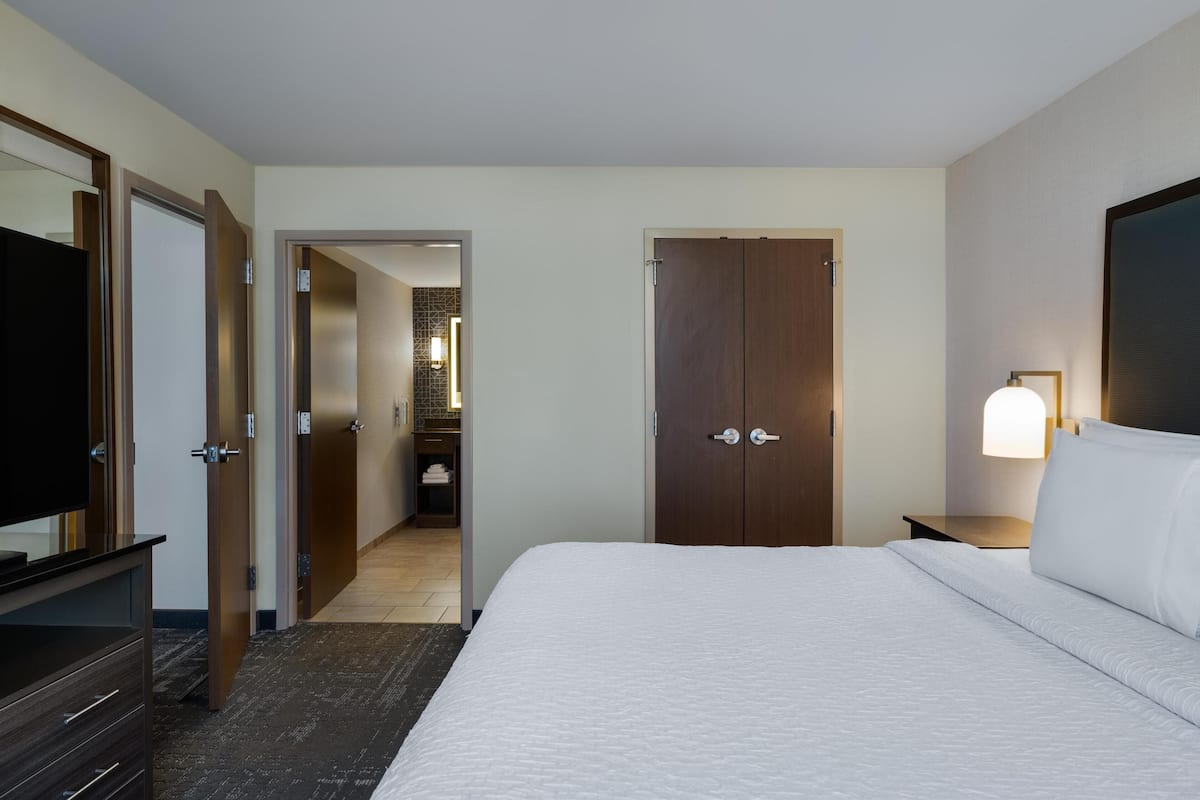 A hotel room with a large bed, a TV, a wardrobe, and a bathroom visible through an open door.