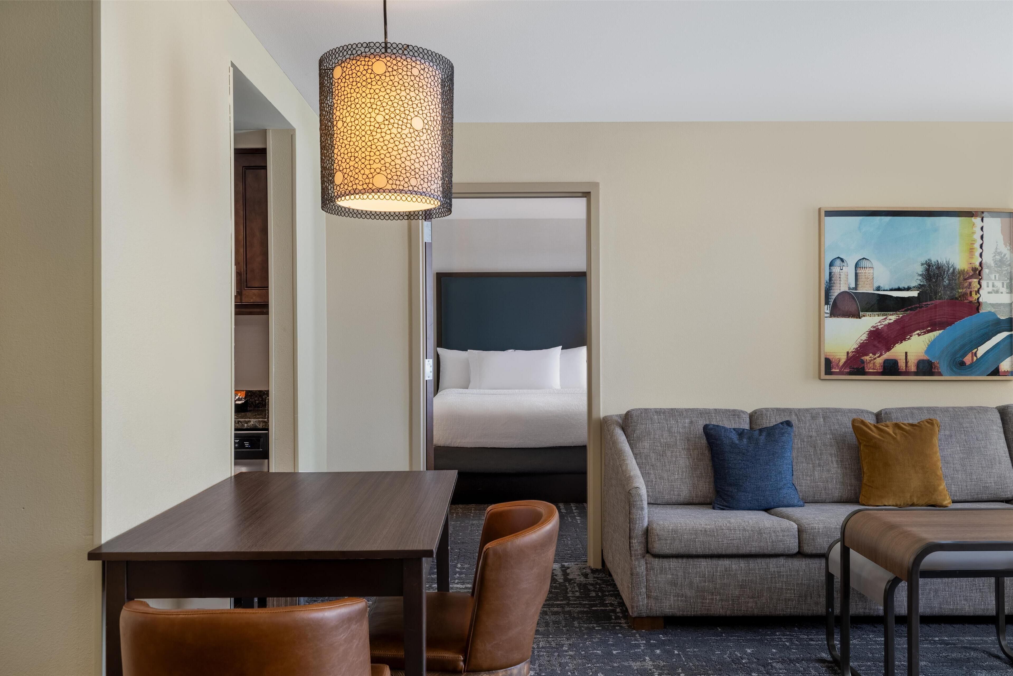 Hotelkamer met een eettafel, twee stoelen, een bank met kussens, een hanglamp en een schilderij aan de muur.