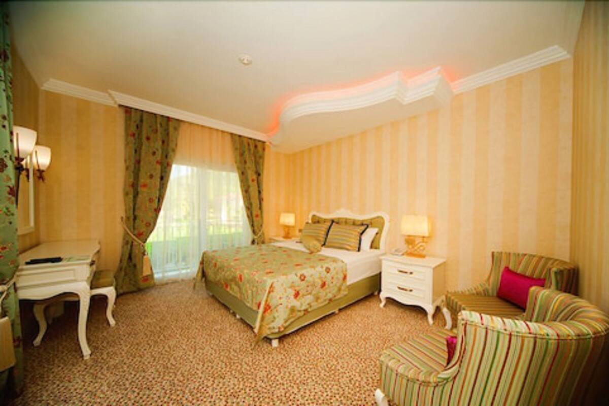 A hotel room with a bed, bedside tables, a desk, a chair, and a window with curtains.