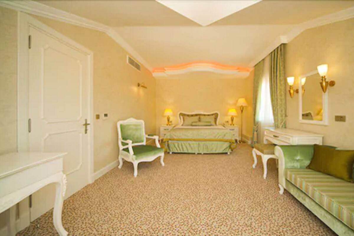 A hotel room with a bed, two bedside tables with lamps, a chair, a sofa, and a desk.