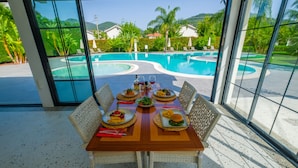 A dining table with a view of a swimming pool and mountains.