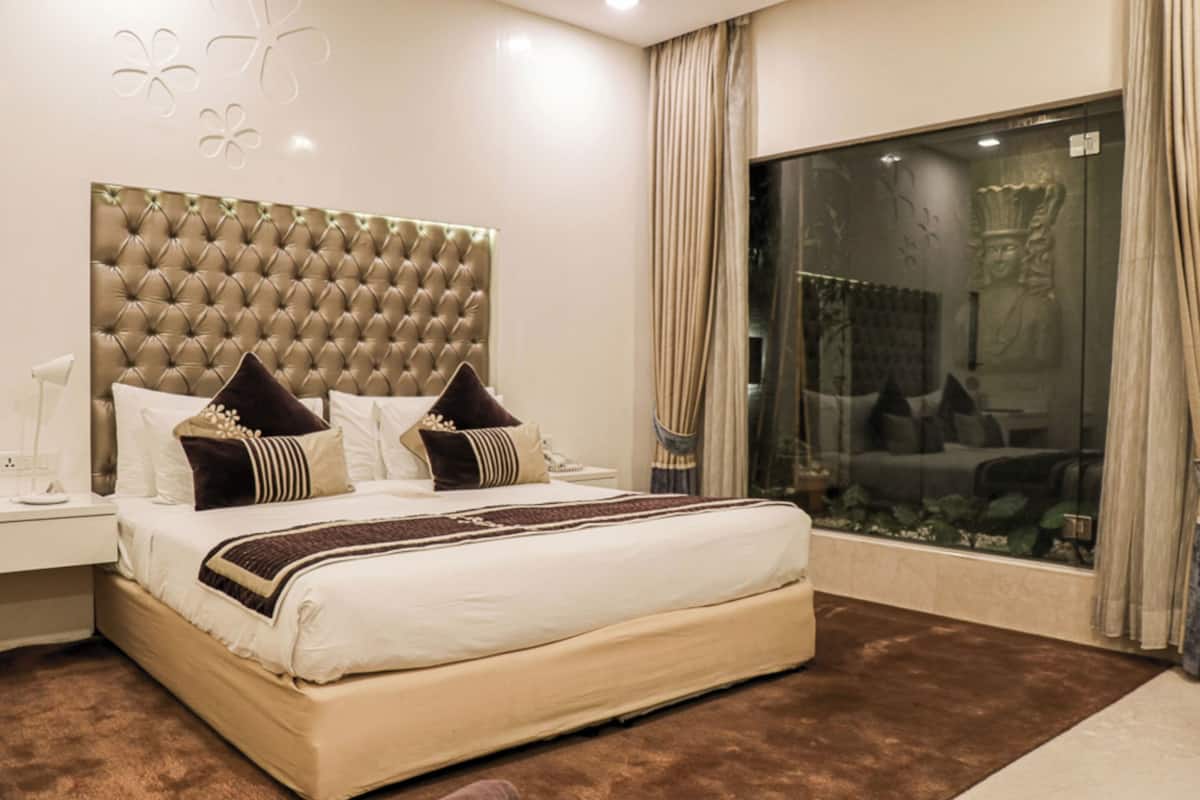 Une chambre à coucher avec un grand lit, une tête de lit capitonnée et une vue sur un jardin, visible à travers une porte vitrée.